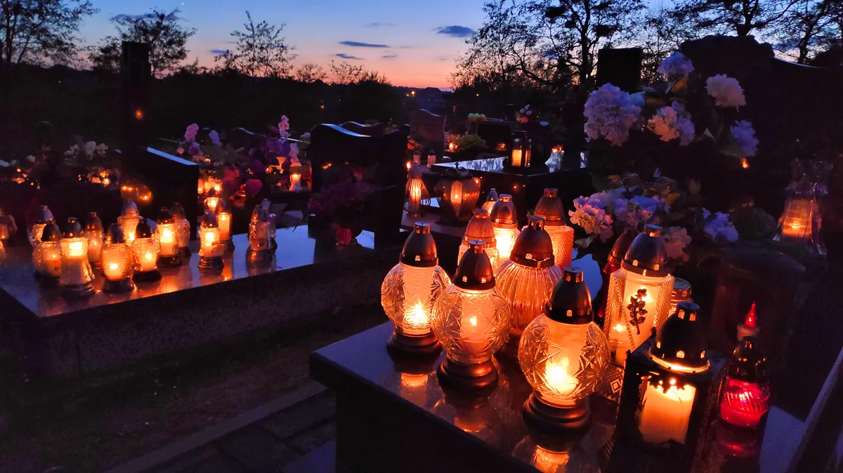 Znicze candles glowing on family graves in a cemetery in Poland at dusk Glass znicze grave candles glowing on family tombs in a Polish cemetery at dusk for All Saints Day