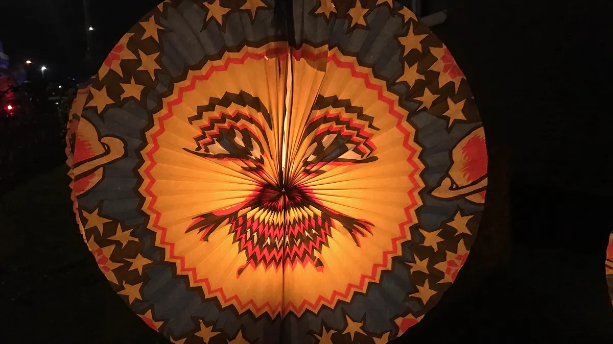 Paper lantern on a Martinslaterne stick lit for a St Martin's Day walk Round paper lantern with a painted face glowing at night during a St Martin's Day lantern walk in Germany