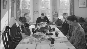 Thanksgiving dinner traditions in 1942: a family bows heads for grace at a long table set with a flower centerpiece in Neffsville, Pennsylvania